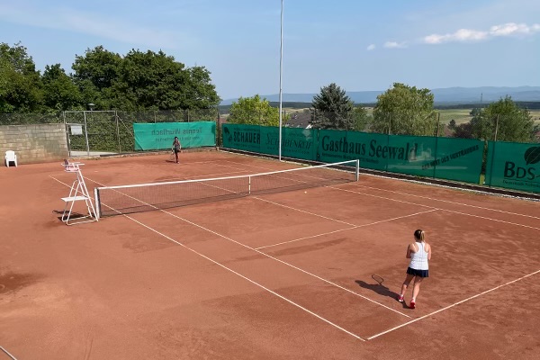 zwei Frauen spielen auf einem Sandplatz ein Tennis-Match